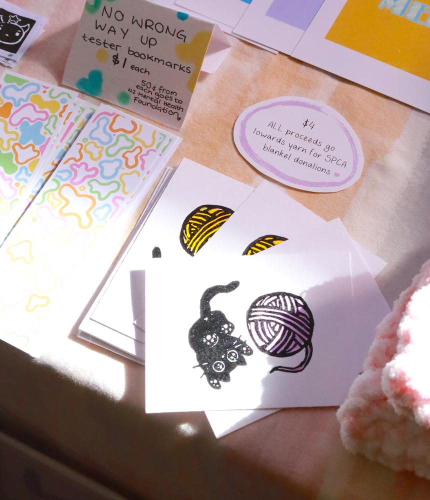 A market stall table, focusing on prints of a black cat playing with a ball of yarn.