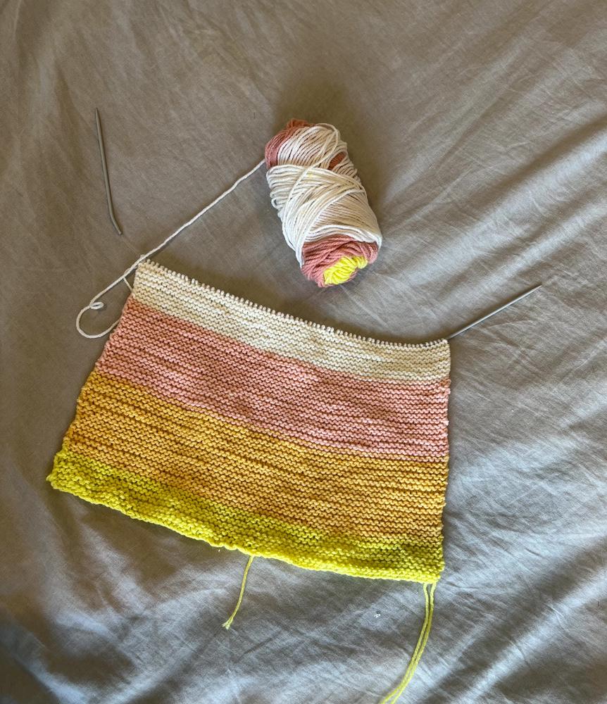 A half-finished yellow, pink, and cream knit blanket.