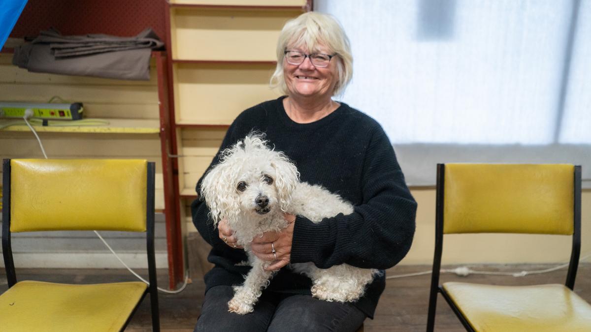 A blonde woman holds an elderly white dog on her lap. Both smile at the camera.