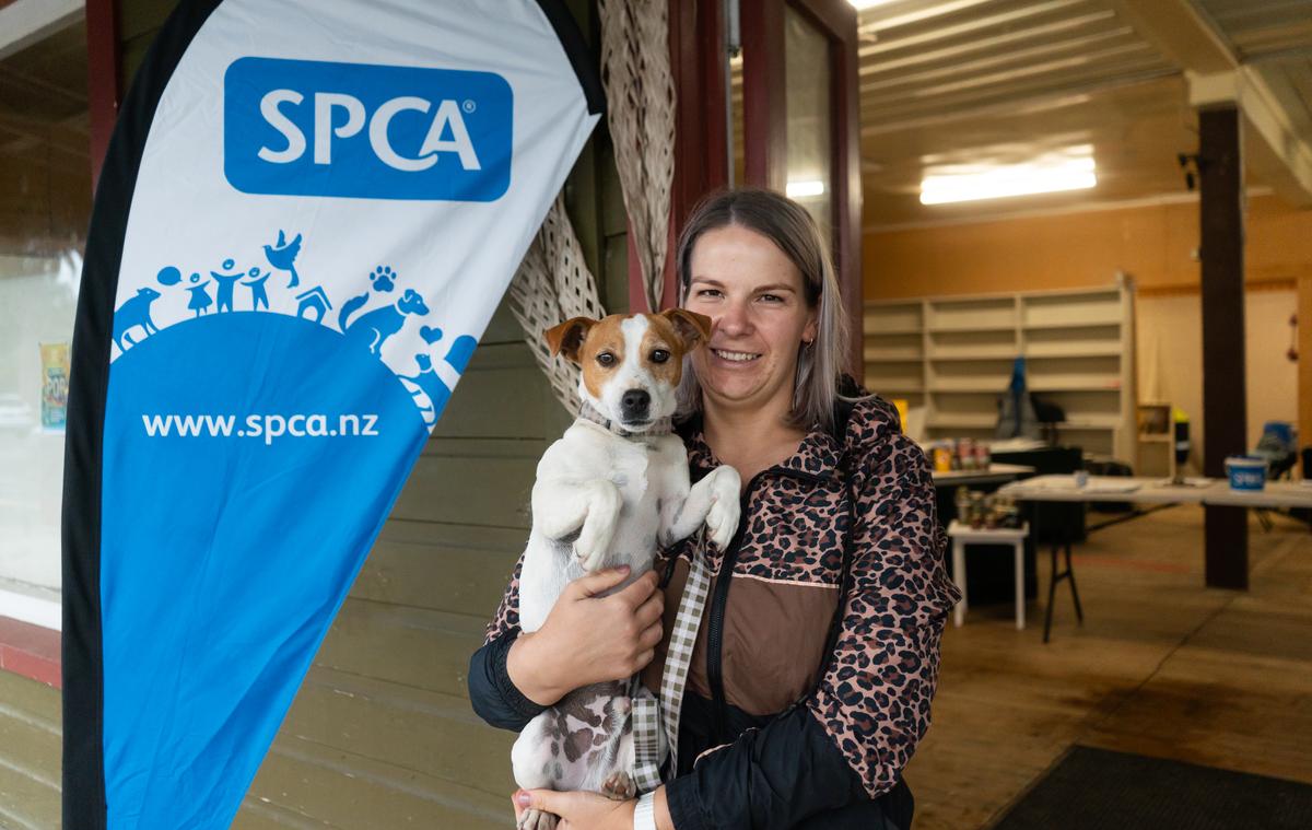 A blonde woman holds a Jack Russell terrier in front of an SPCA sign.