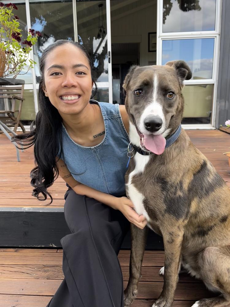 A woman sits on a deck with a brown and white dog, smiling.